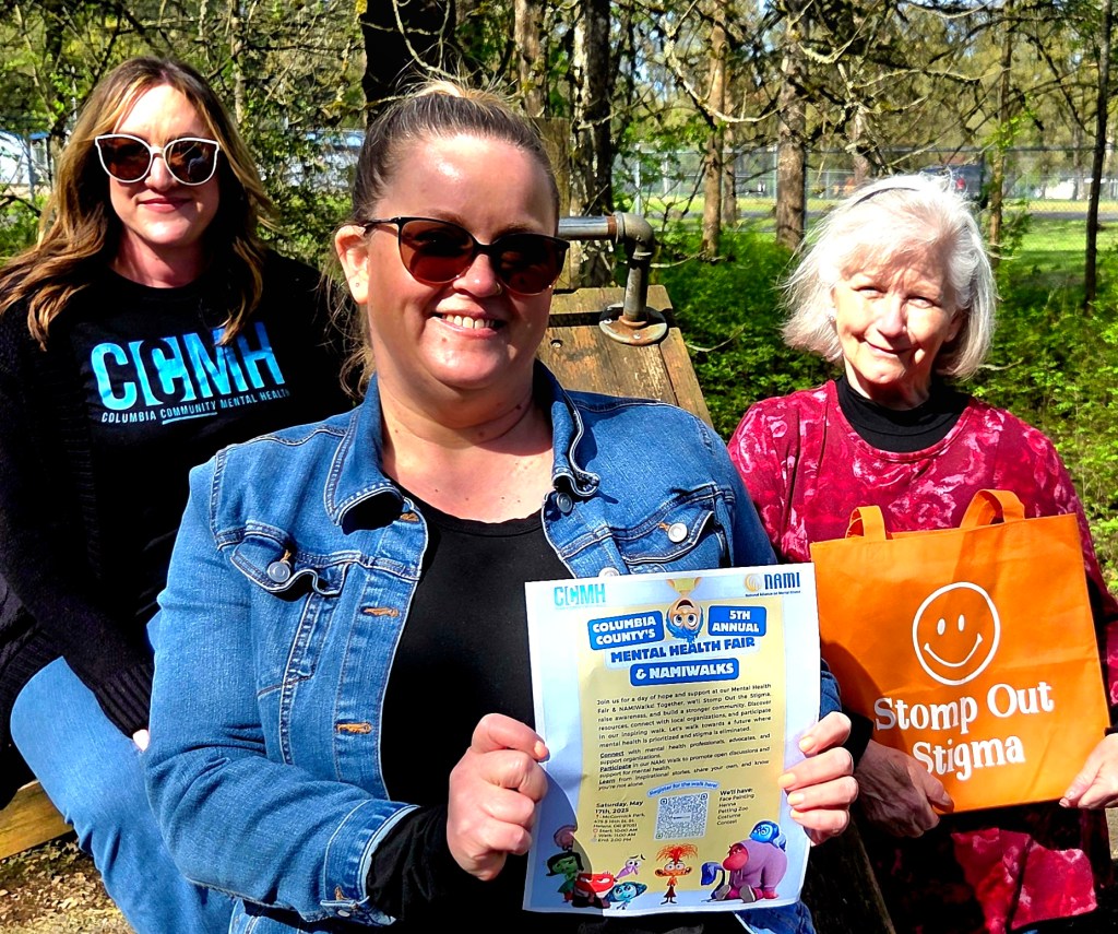Columbia County Mental Health's Trish Tyler and Heather Petersen pose with National Alliance on Mental Illness's Judy Thompson holding flyers and merchandise for the Columbia County Mental Health Fair.